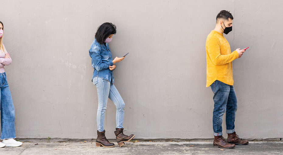 People standing in a socially distanced queue wearing masks and looking at their mobile phones